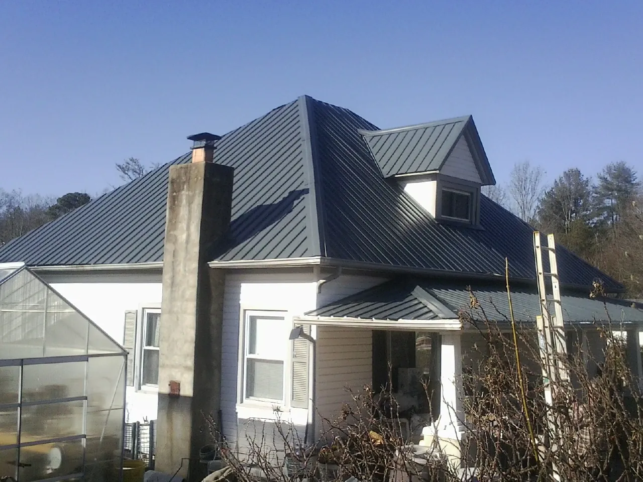 Dark blue standing seam metal roof on a white farmhouse with dormer — Slate & Tile Roof Repair by Roofing Brothers in New Hyde Park