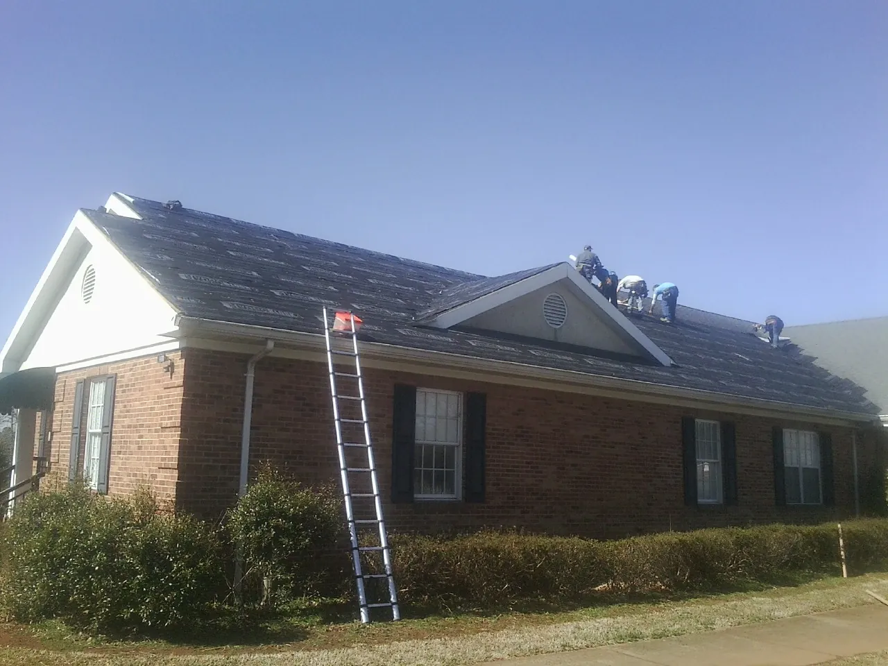 Crew tearing shingles off a brick ranch roof with a ladder set — Metal Roof Repair work by our crew in New Hyde Park