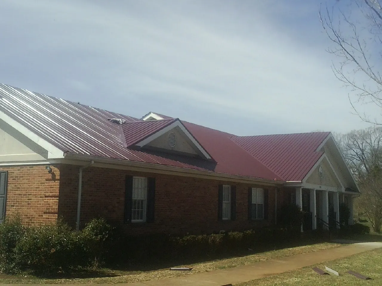 Red metal roof with gabled entries on a long brick building, from a Hail Damage Roof Repair job in New Hyde Park
