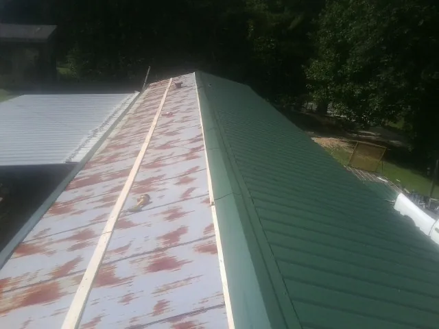Old rusted panels beside newly installed green metal roofing — Wind Damage Roof Repair by Roofing Brothers in New Hyde Park
