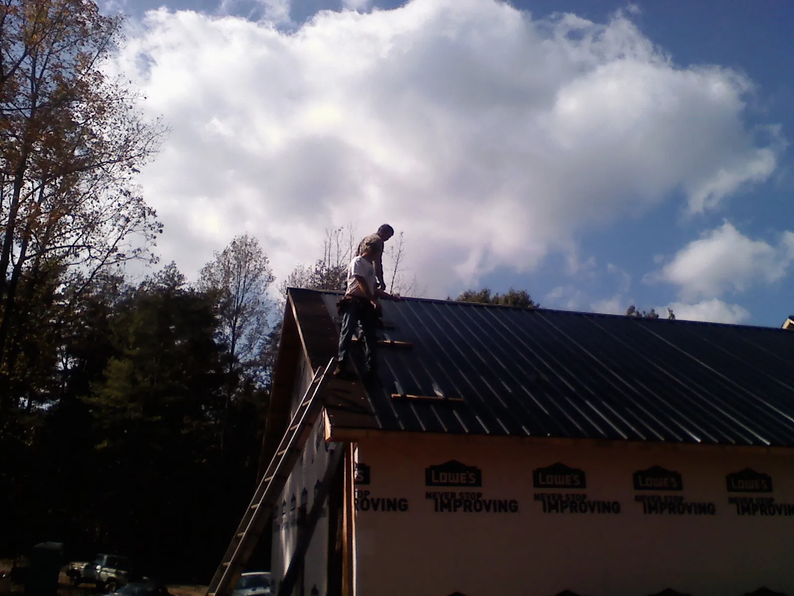 Roofer fastening dark metal panels high against a cloudy sky, from a Roof Inspection job in New Hyde Park