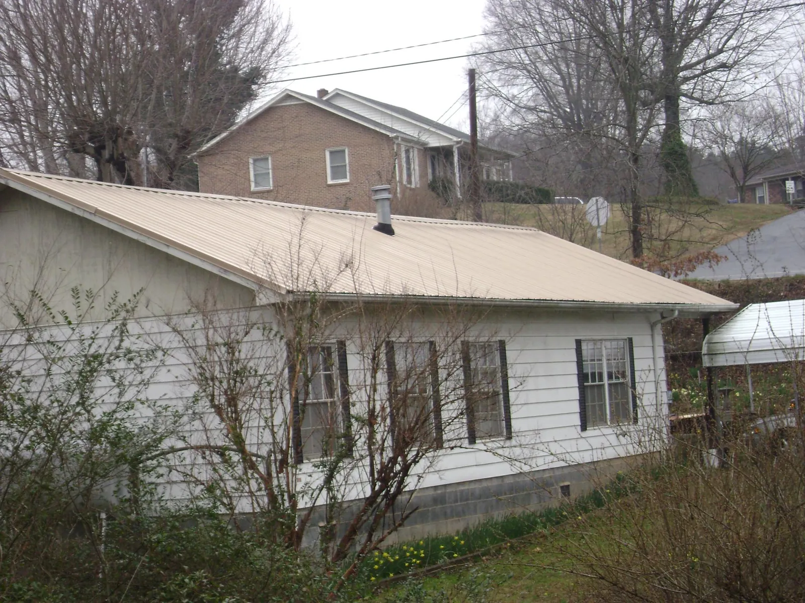 Tan metal roof on a white sided house set into a hillside — Commercial Roofing by Roofing Brothers in New Hyde Park