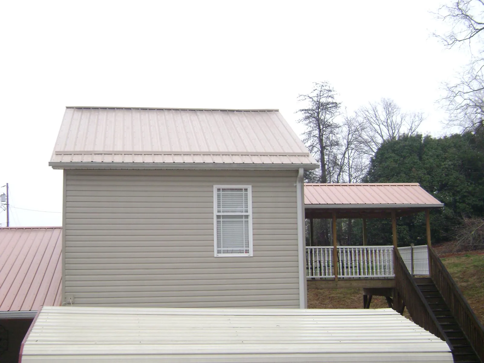 Tan metal roofs on a two story addition and attached porch, from a Roof Replacement job in New Hyde Park